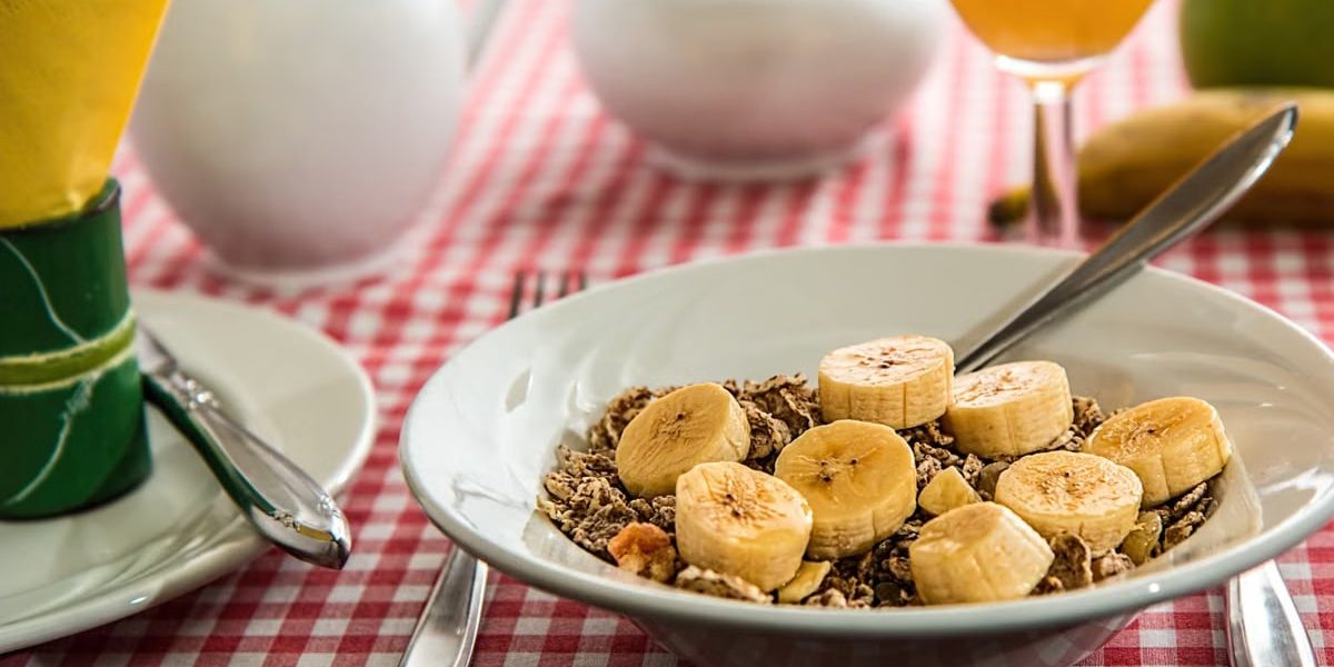 A healthy breakfast bowl with sliced bananas and cereal on a red checkered tablecloth.