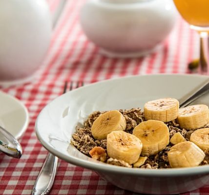A healthy breakfast bowl with sliced bananas and cereal on a red checkered tablecloth.