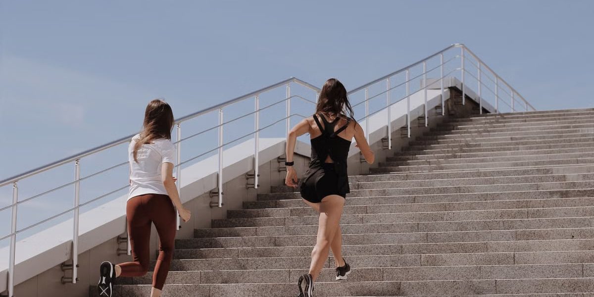 Two women running up stairs outdoors, embodying fitness and wellness.