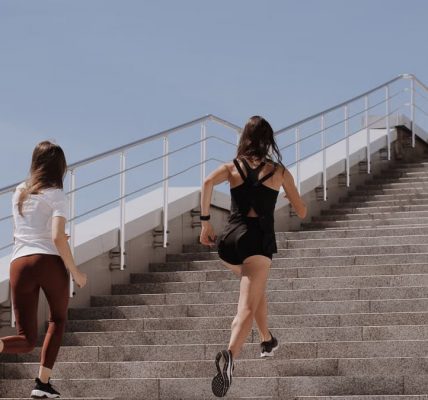 Two women running up stairs outdoors, embodying fitness and wellness.